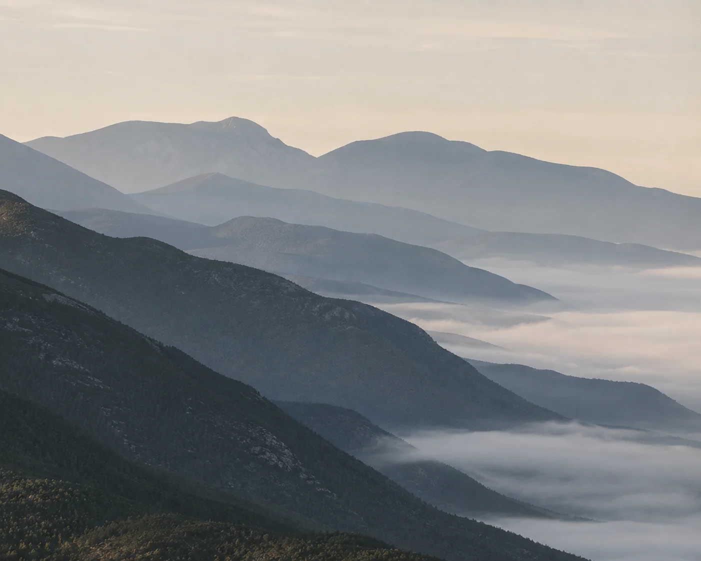 Layered mountain ridgelines receding into low cloud at first light